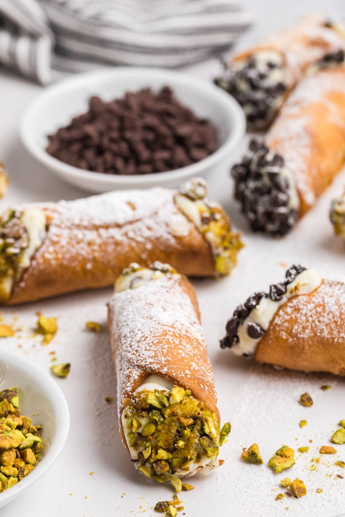 Four cannoli with cream filling, dipped in pistachios or chocolate chips, dusted with powdered sugar.