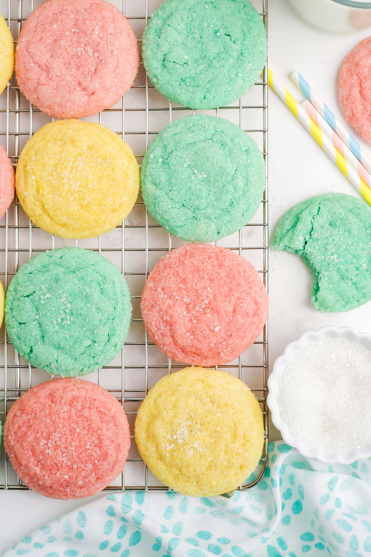 Kool-Aid Cookies&mdash;colorful sugar cookies in pink, yellow, and green&mdash;cooling on a wire rack, with sugar and straws nearby.