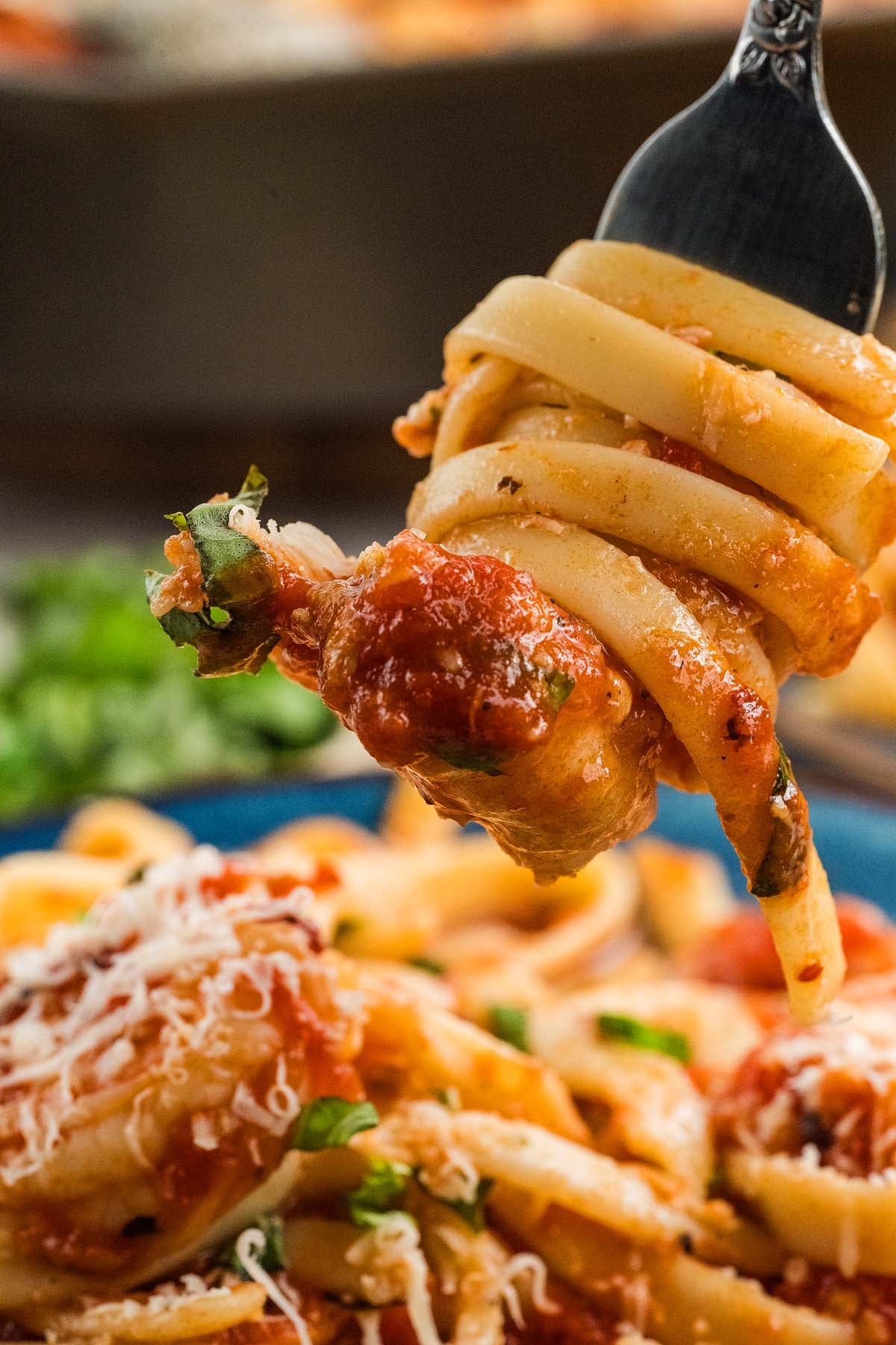 A fork twirls shrimp fra Diavolo pasta with tomato sauce and herbs above a plate topped with grated cheese.