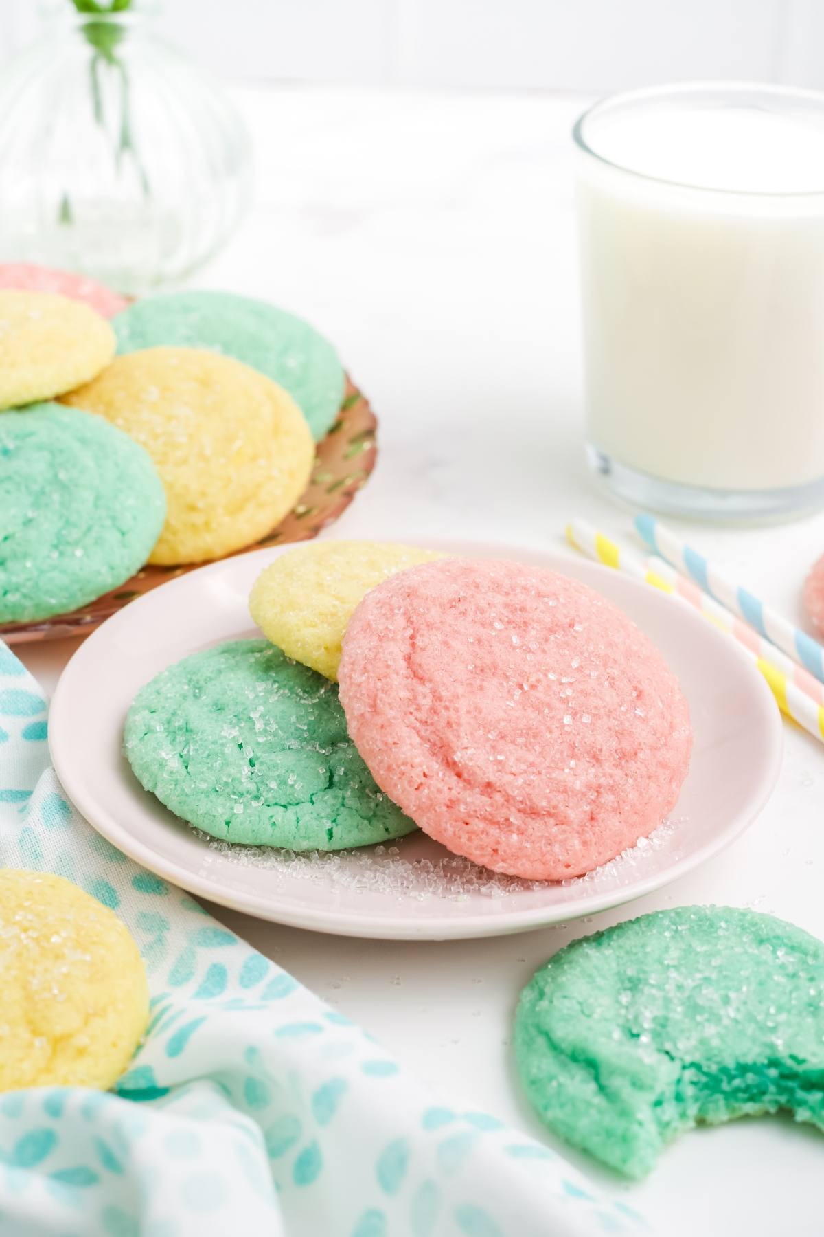 Colorful pastel sugar Kool-Aid cookies on a plate with a glass of milk in the background.