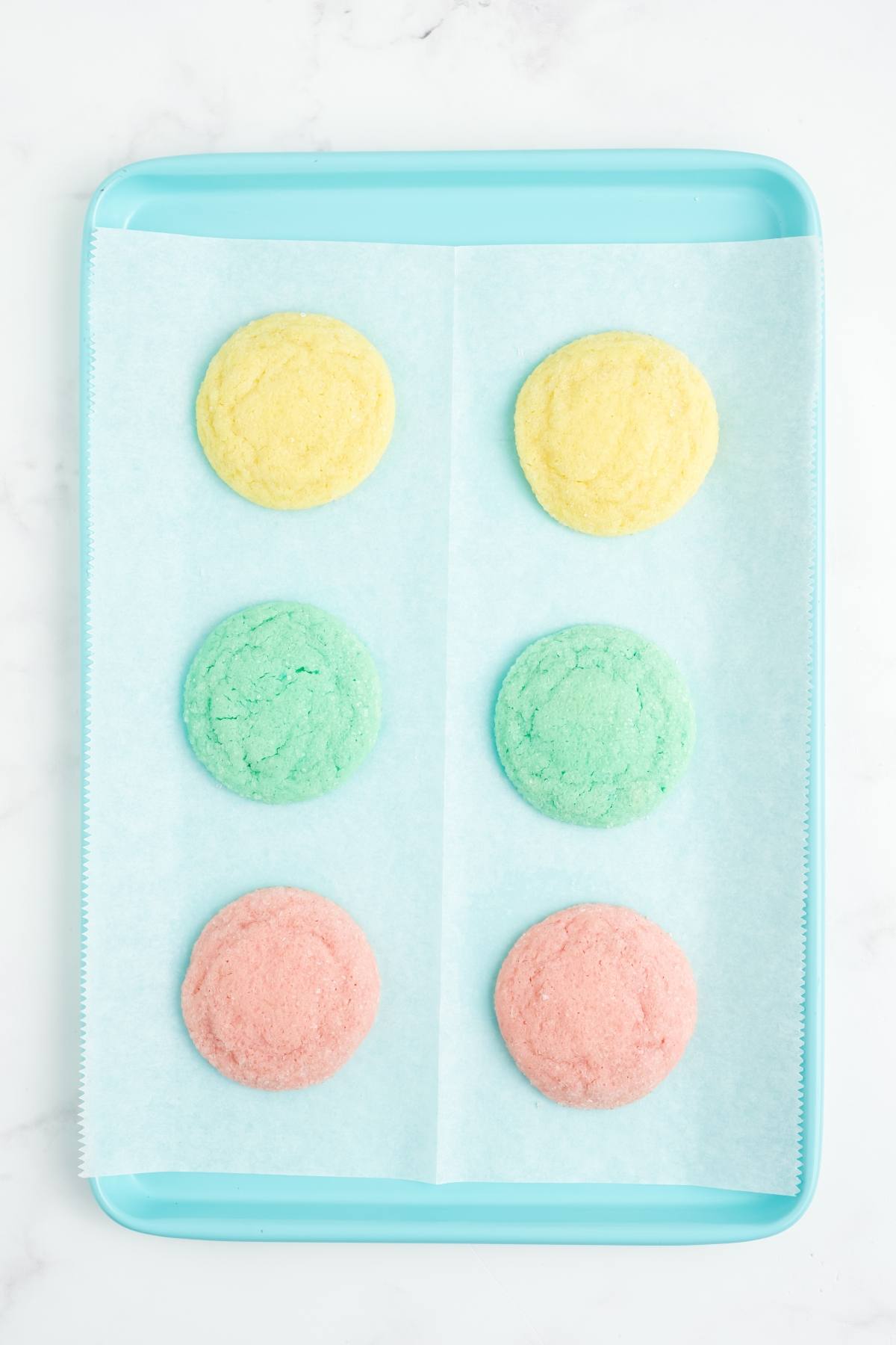 Three rows of pastel yellow, green, and pink cookies on a blue tray lined with parchment paper.