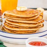 A stack of McDonalds Copycat Pancakes with butter on top, served on a plate with a fork and condiments nearby.