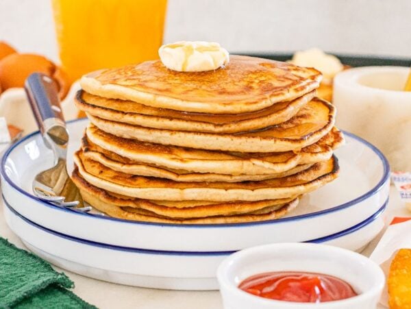 A stack of McDonalds Copycat Pancakes with butter on top, served on a plate with a fork and condiments nearby.