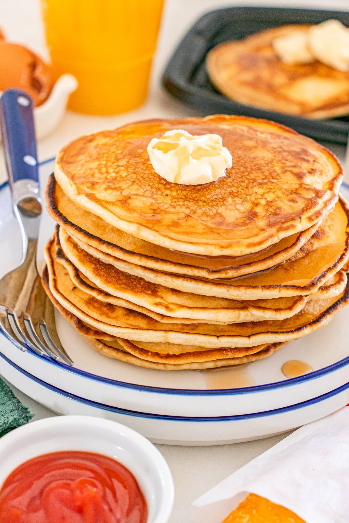 A stack of McDonald's copycat pancakes topped with butter on a plate, with breakfast items and syrup in the background.