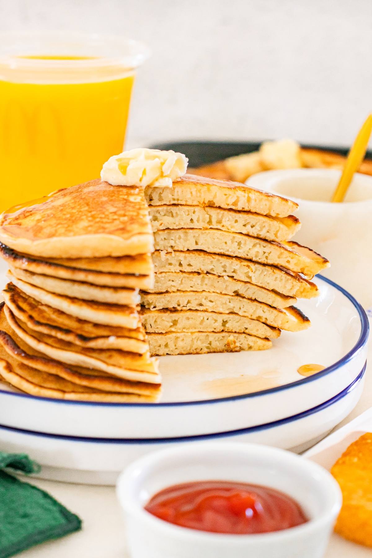 A stack of sliced McDonalds copycat pancakes with butter on top, served with syrup and a glass of orange juice in the background.