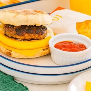 Breakfast sandwich with sausage, egg, and cheese on an English muffin, just like a McDonalds Copycat Sausage Egg McMuffin, served with hash browns and ketchup.