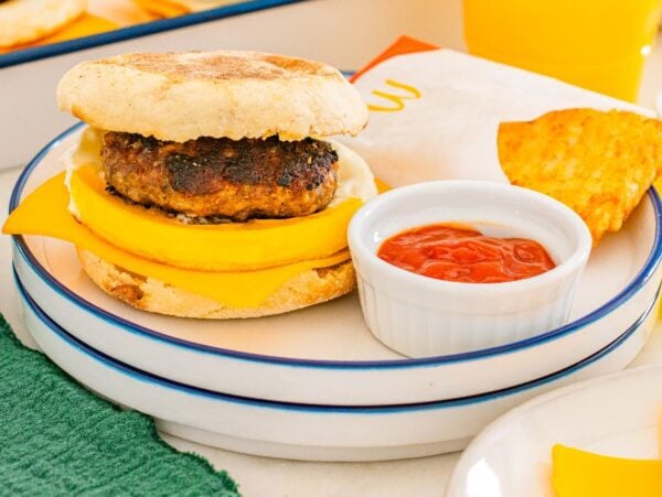 Breakfast sandwich with sausage, egg, and cheese on an English muffin, just like a McDonalds Copycat Sausage Egg McMuffin, served with hash browns and ketchup.