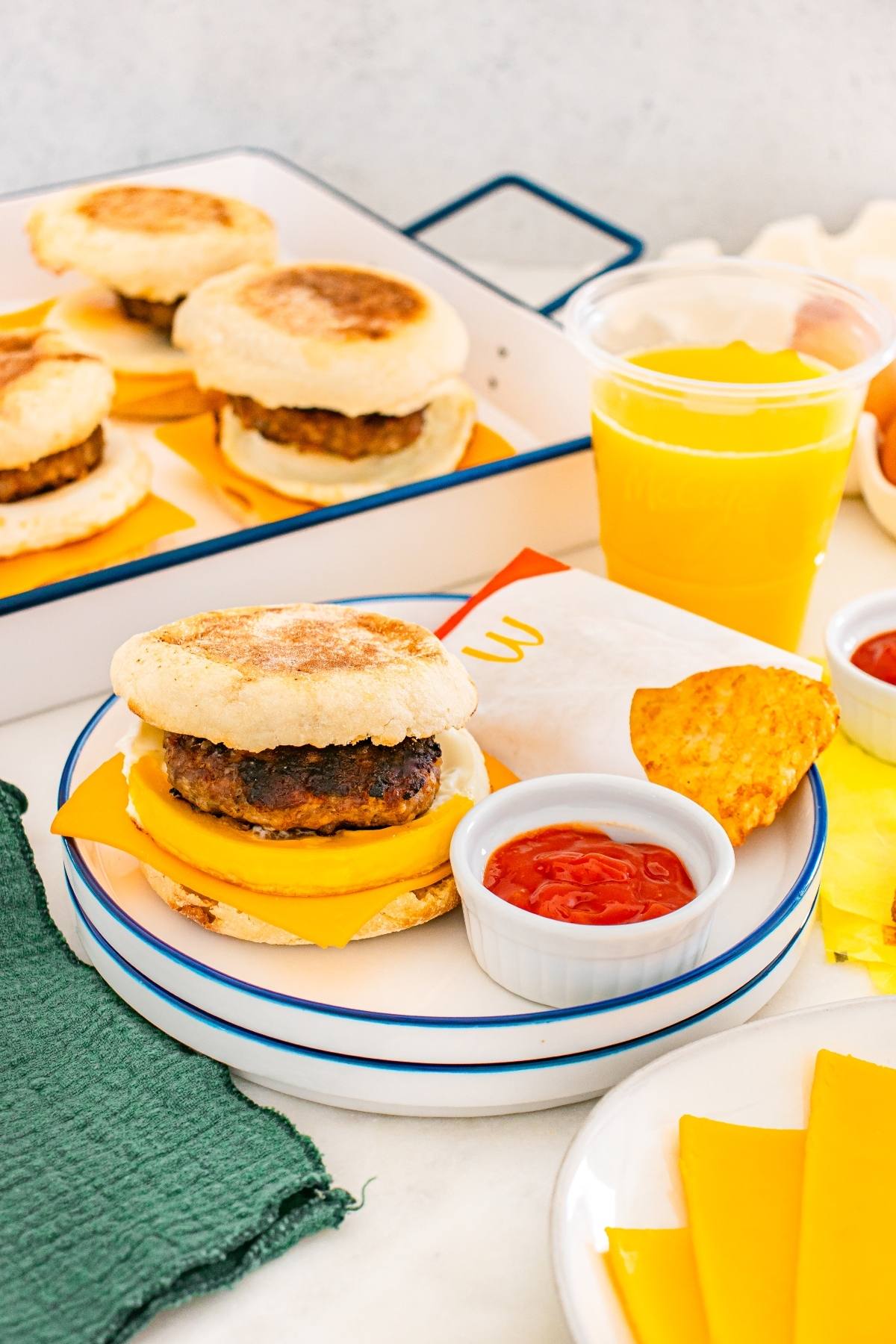 Breakfast sandwich with sausage, egg, and cheese on an english muffin with orange juice and ketchup on the side.
