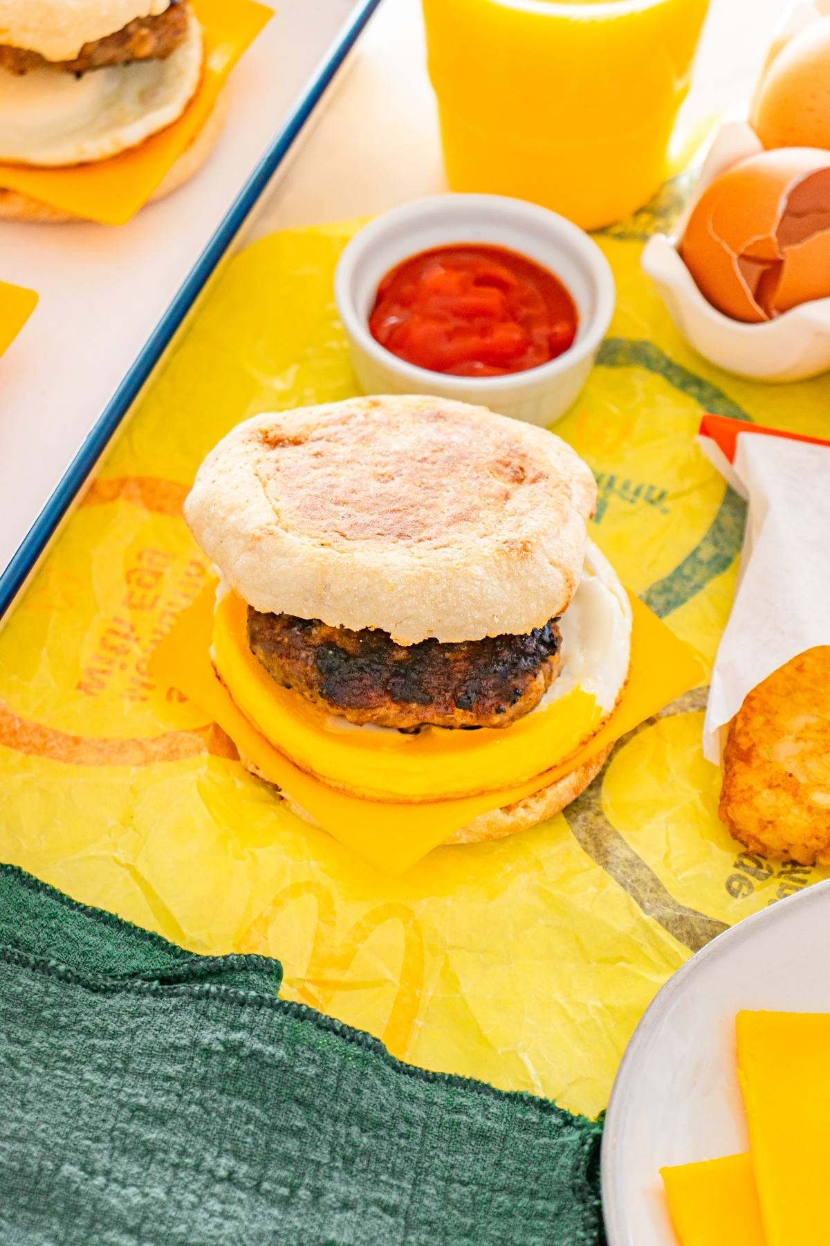 Breakfast sandwich with sausage, egg, and cheese on an english muffin, next to ketchup and hash brown.