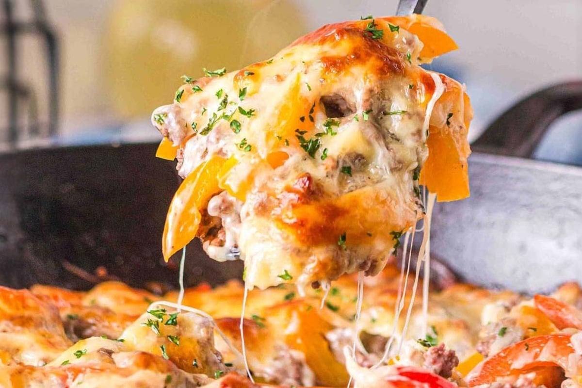 Cheesy casserole with ground meat, bell peppers, and herbs being served from a skillet.