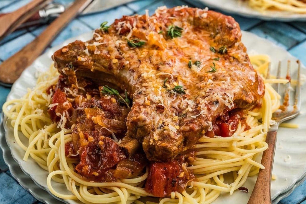Pork chop with tomato sauce served over spaghetti, garnished with herbs and grated cheese on a plate.
