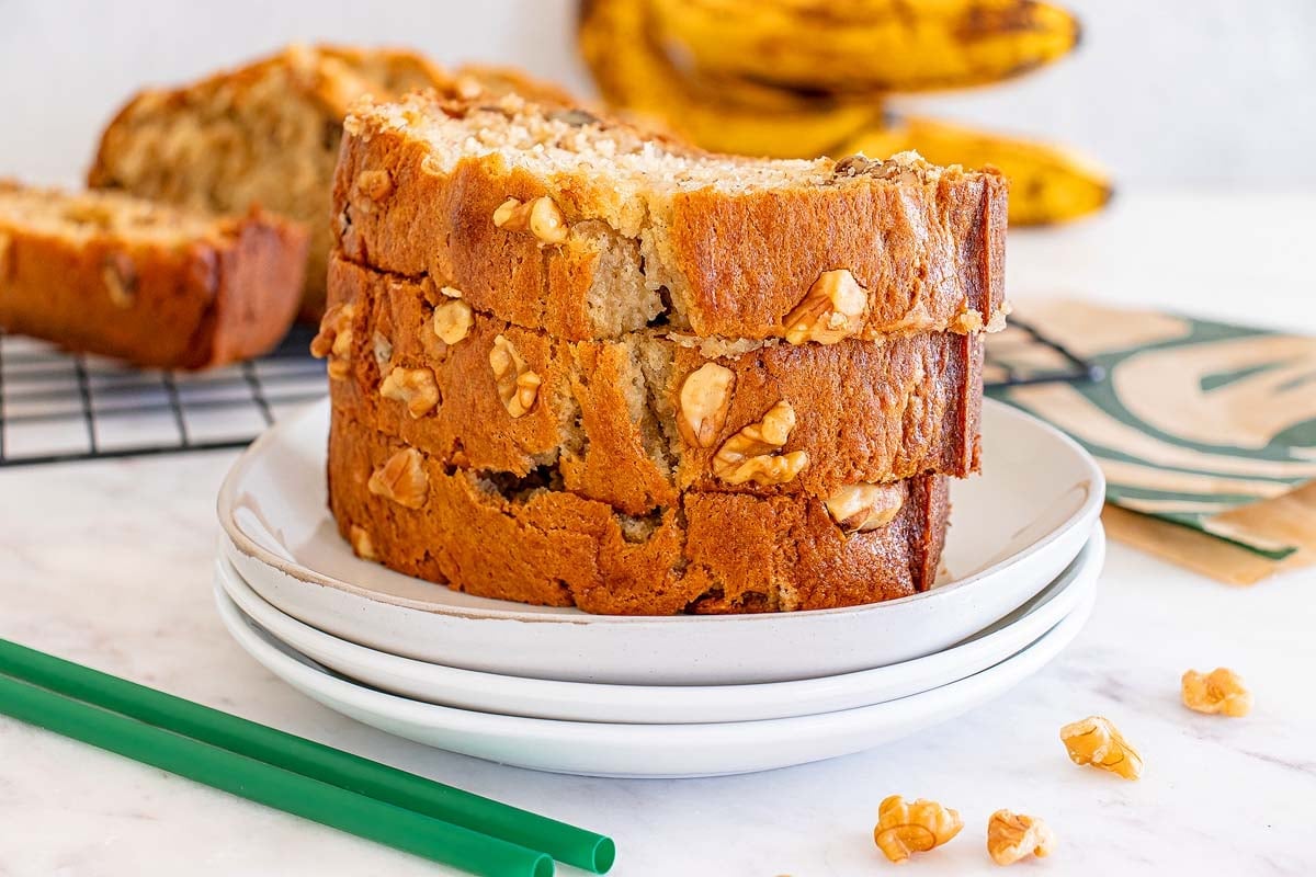 Sliced banana nut bread on a white plate, with banana and more bread in the background.