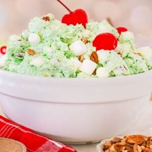 A white bowl of Watergate Salad&mdash;green pistachio fluff with marshmallows, nuts, and cherries on top&mdash;sits next to Jell-O boxes.