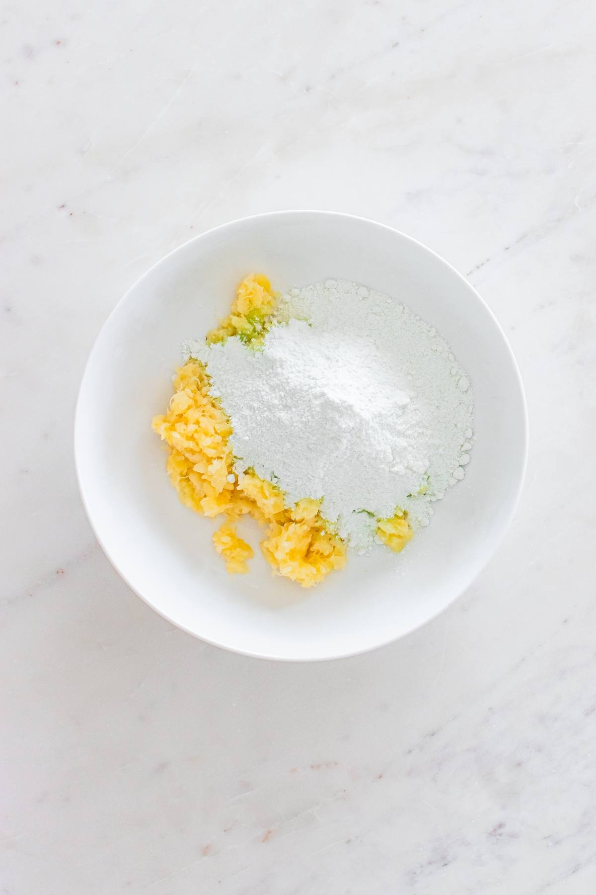 A white bowl with chopped butter and flour on a white marble surface.