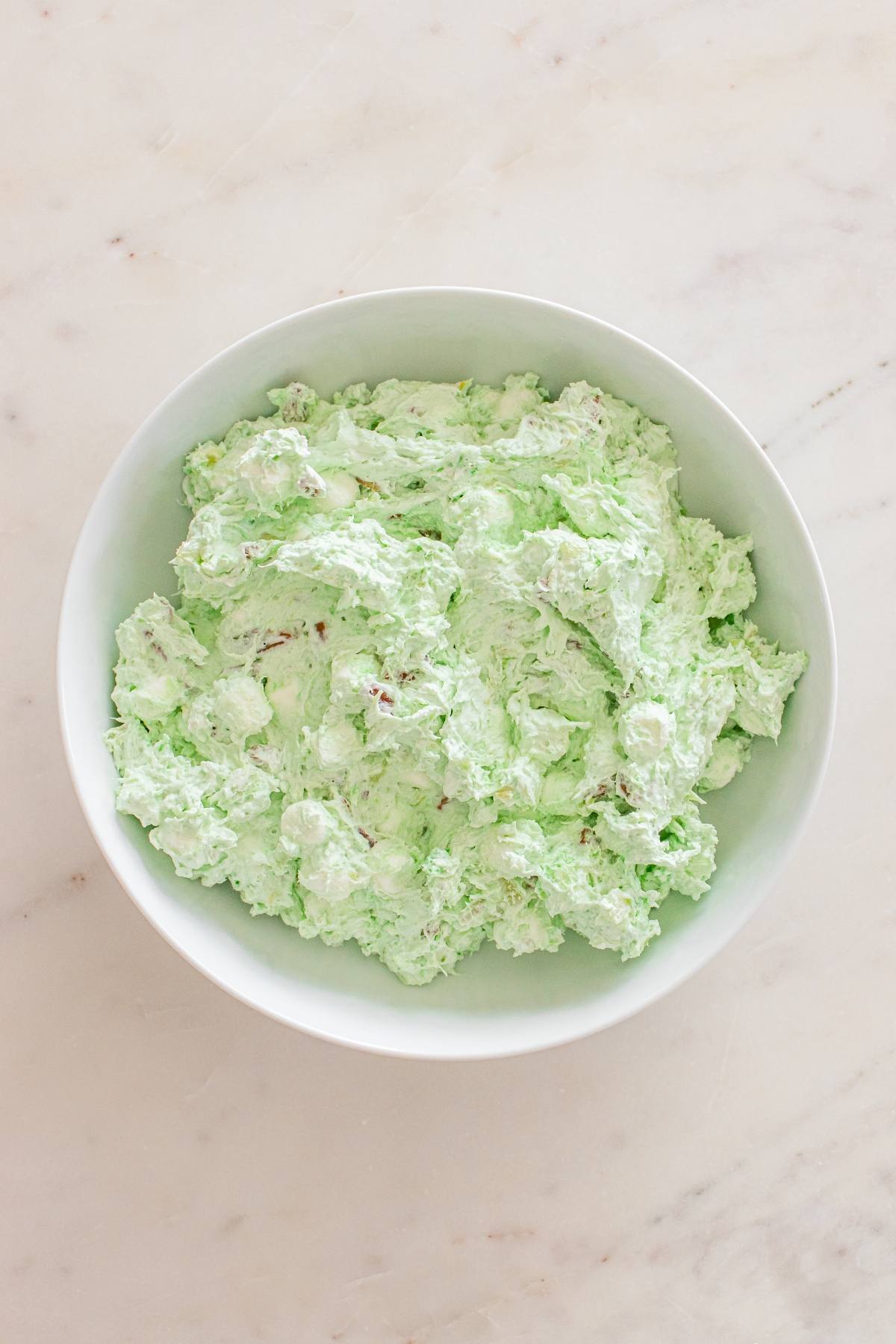 A white bowl filled with light green, fluffy whipped salad on a marble surface.