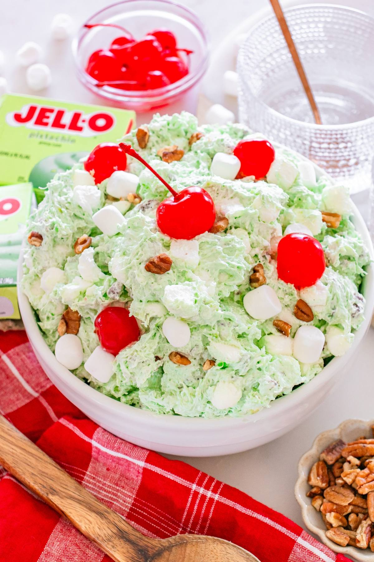A bowl of Watergate salad with cherries, mini marshmallows, and pecans, on a red cloth.
