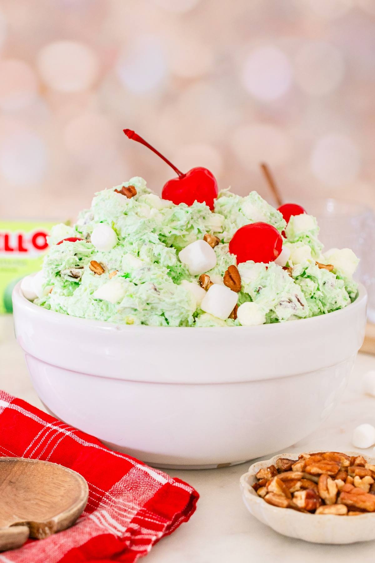 A white bowl of Watergate salad  with marshmallows, pecans, and cherries on top.