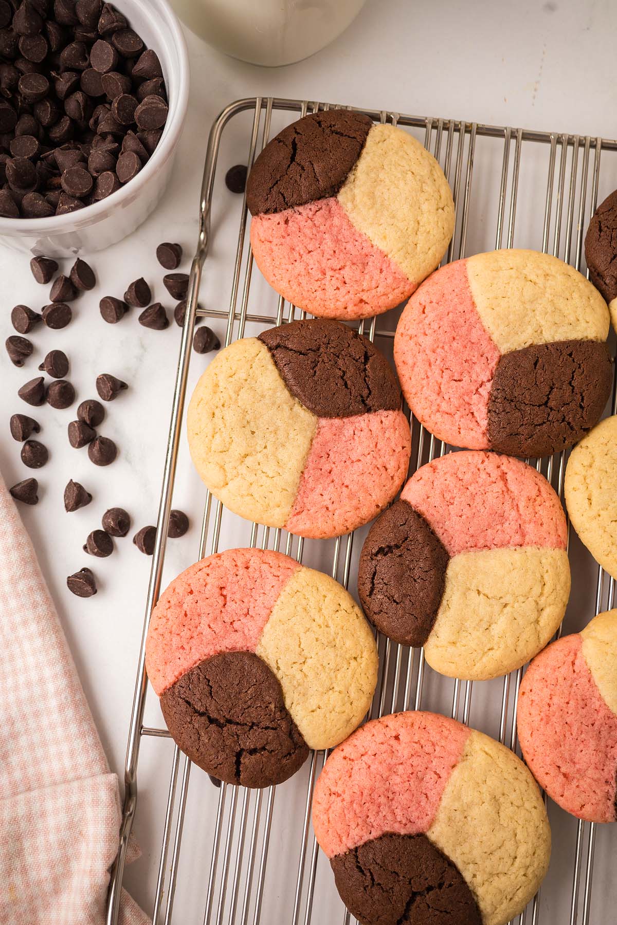 Neapolitan Cookies with chocolate, vanilla, and pink sections cool on a wire rack near scattered chocolate chips.
