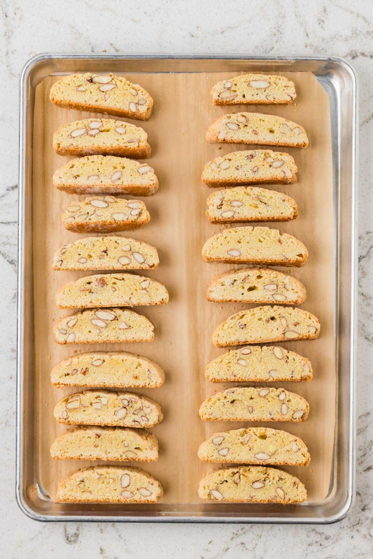 Rows of almond biscotti slices arranged neatly on a parchment-lined baking sheet.