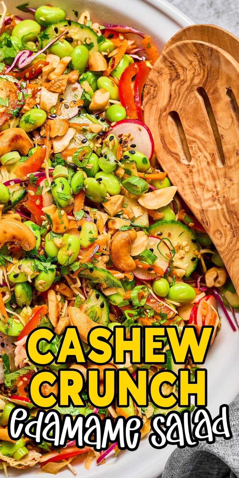 Colorful Cashew Crunch Edamame Salad with chopped veggies, fresh herbs, and a wooden serving spoon in a white bowl.