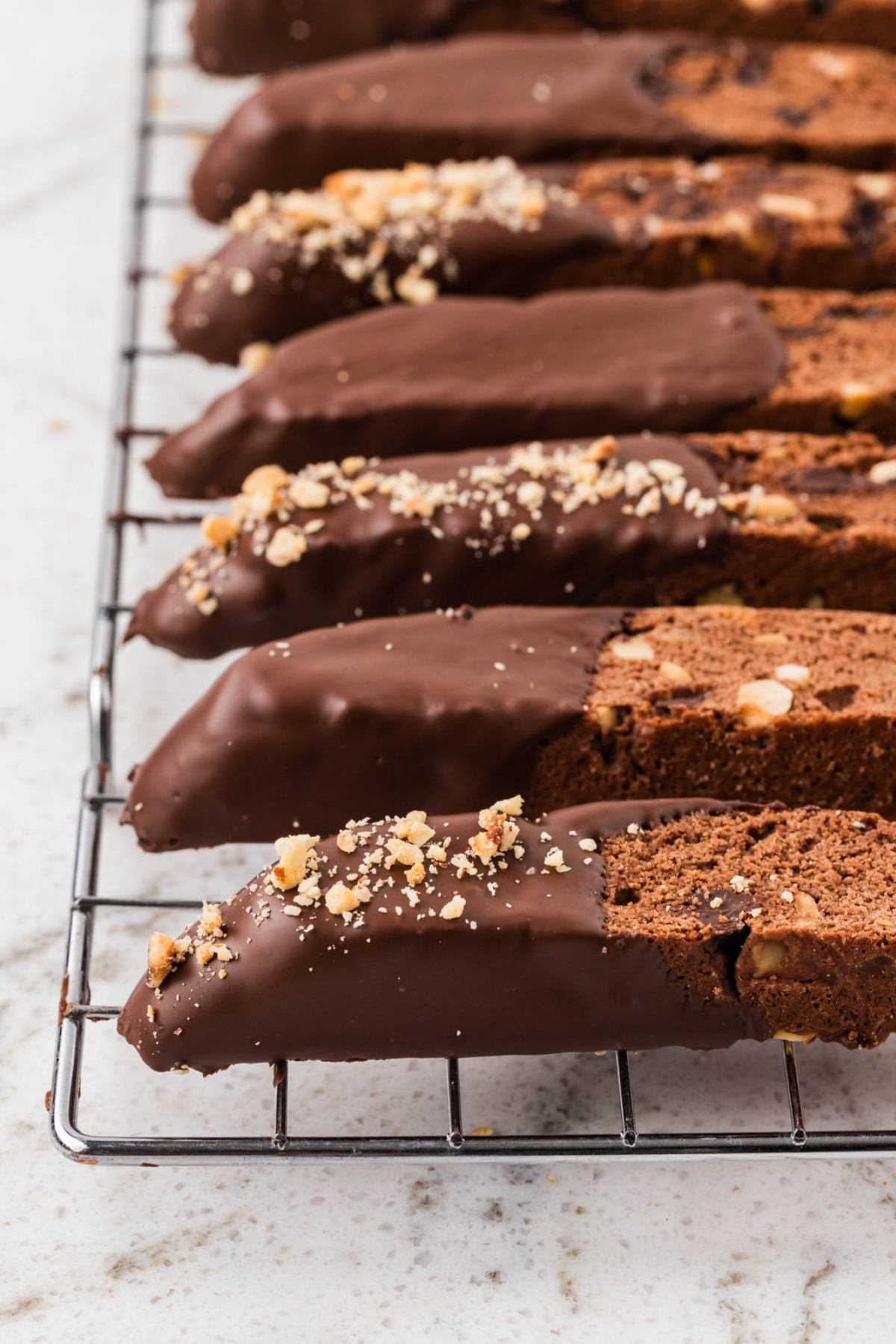Chocolate-dipped biscotti with chopped nuts on top, cooling on a wire rack.