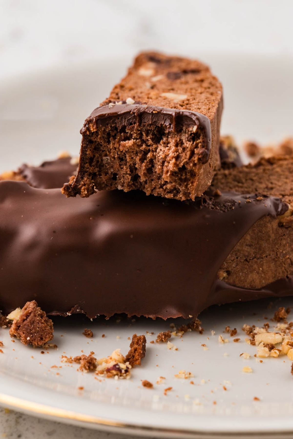 Two chocolate-dipped biscotti on a plate, one stacked with a bite taken out, with crumbs around.