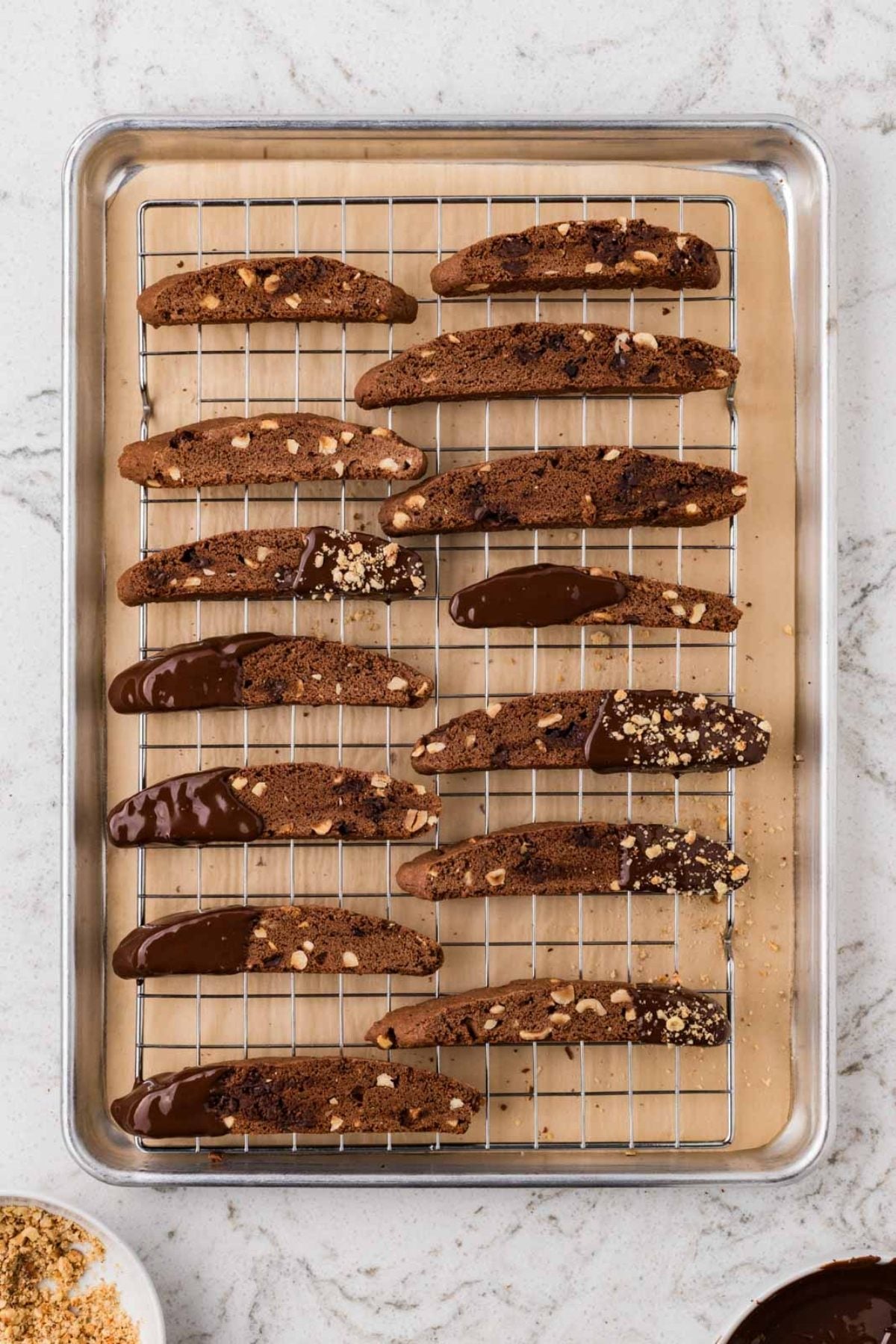 Rows of chocolate-dipped biscotti with nuts cooling on a wire rack over a baking tray.
