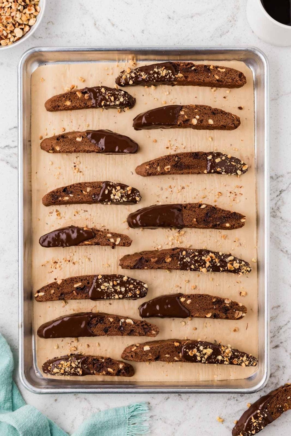 Rows of chocolate-dipped biscotti with nuts on a parchment-lined baking sheet, seen from above.