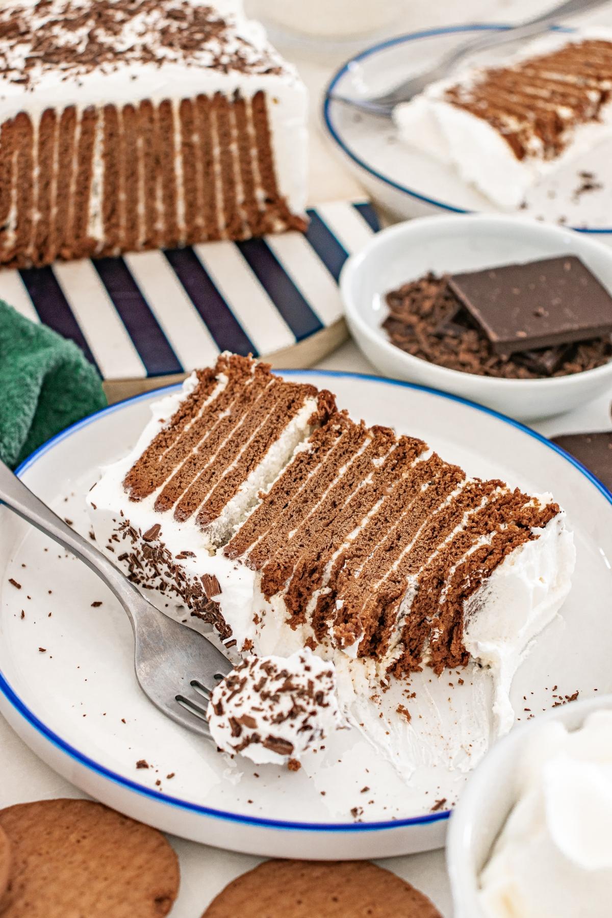 A slice of Chocolate icebox cake with chocolate layers and whipped cream on a plate, garnished with chocolate shavings.