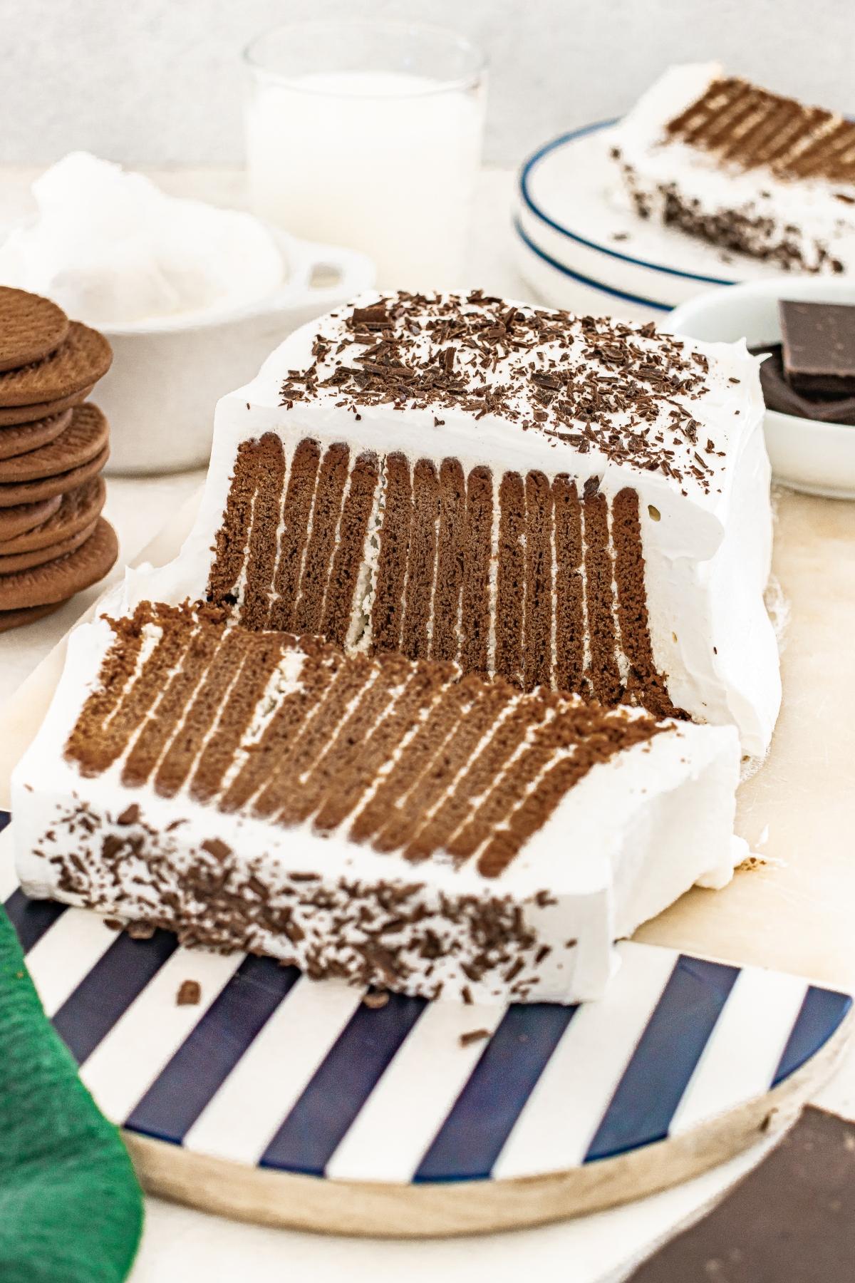 Chcolate icebox cake with  cookies and whipped cream, sliced on a striped plate with chocolate shavings.