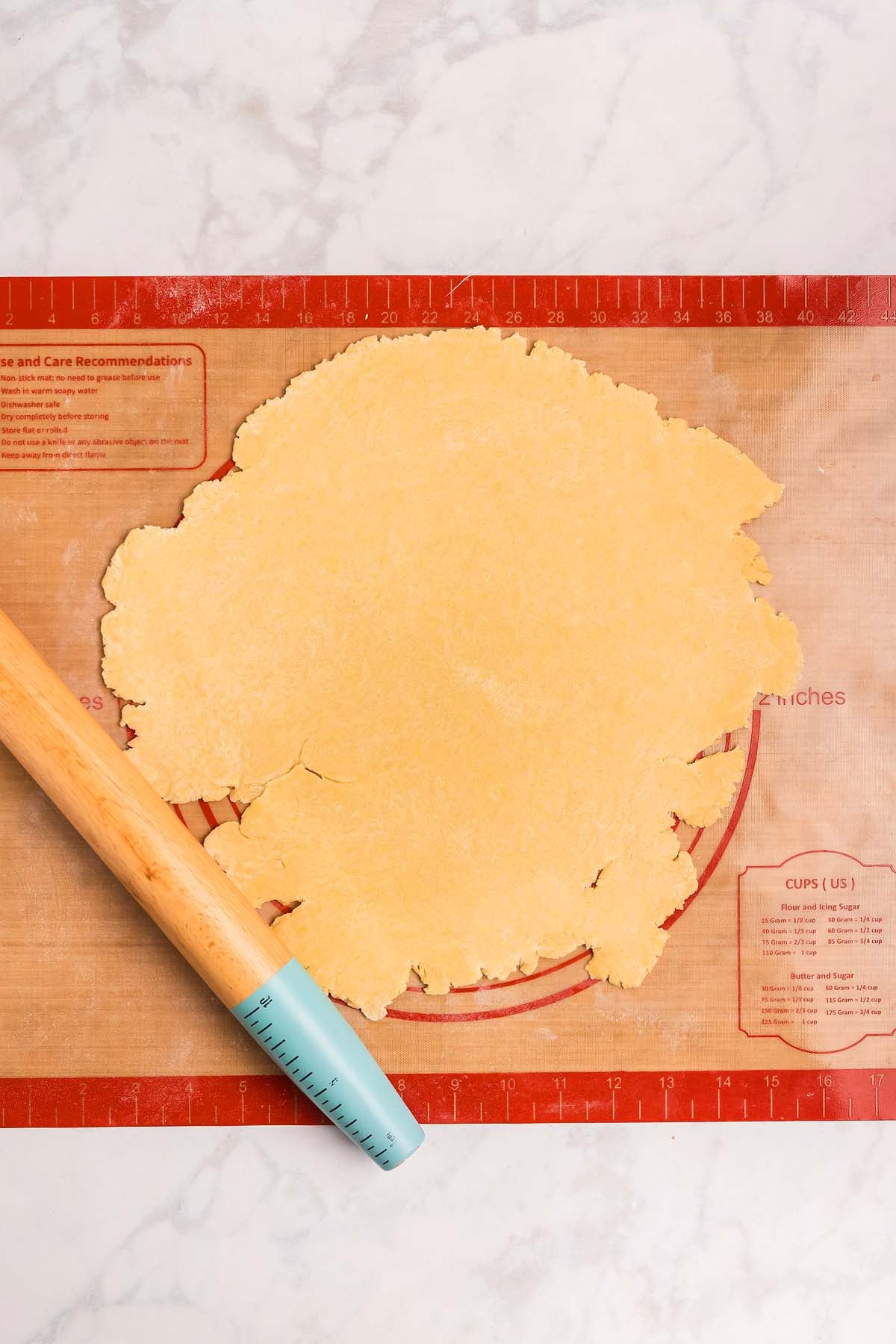 Unbaked pie crust rolled out on a silicone baking mat with a rolling pin on a marble counter, ready to be transformed into homemade cannoli or your favorite pastry.