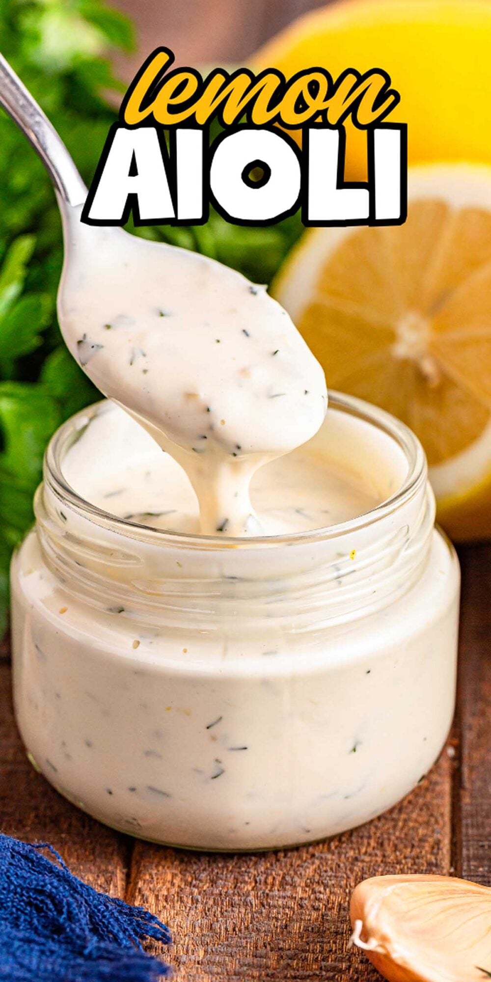 A spoon scooping rich Lemon Aioli from a glass jar, with fresh lemons and parsley in the background.