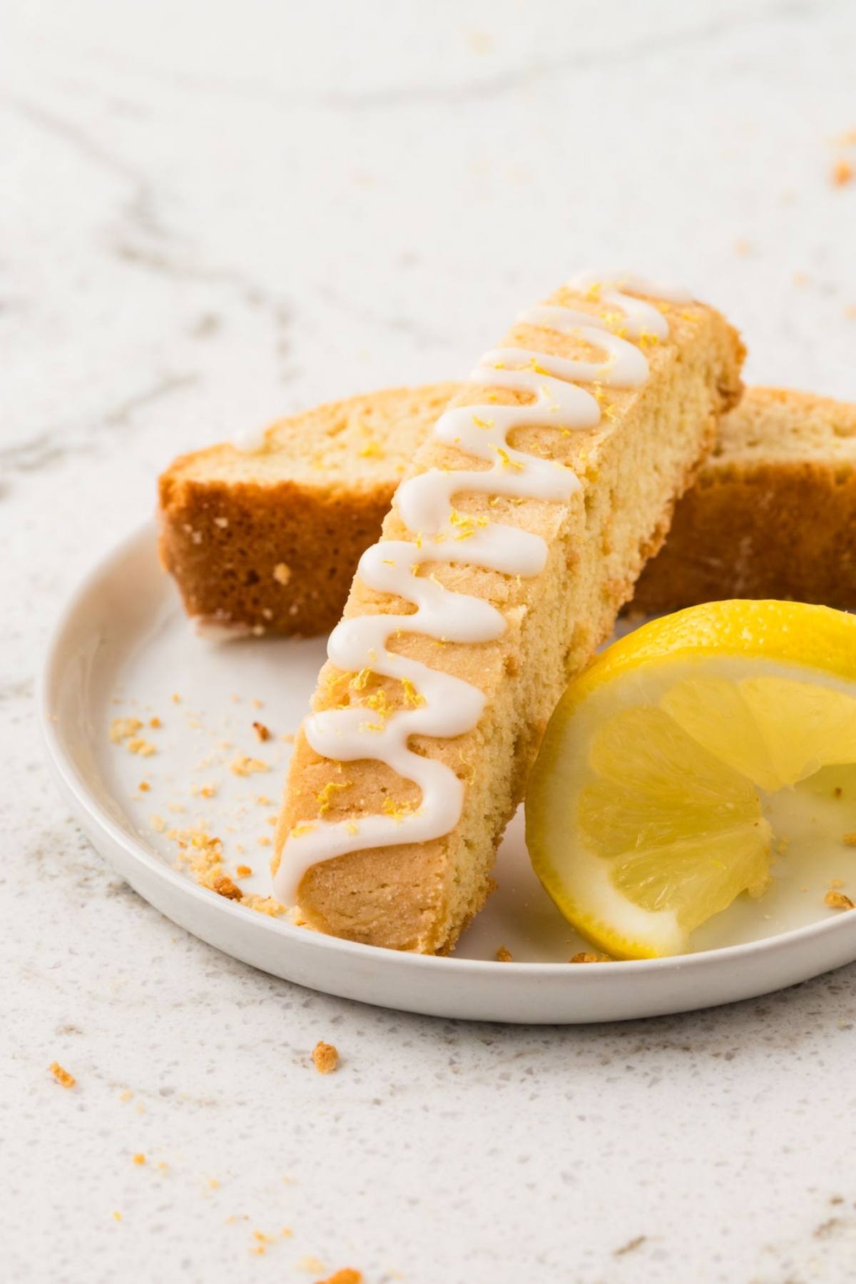 A lemon biscotti with white icing and a lemon wedge on a small white plate.