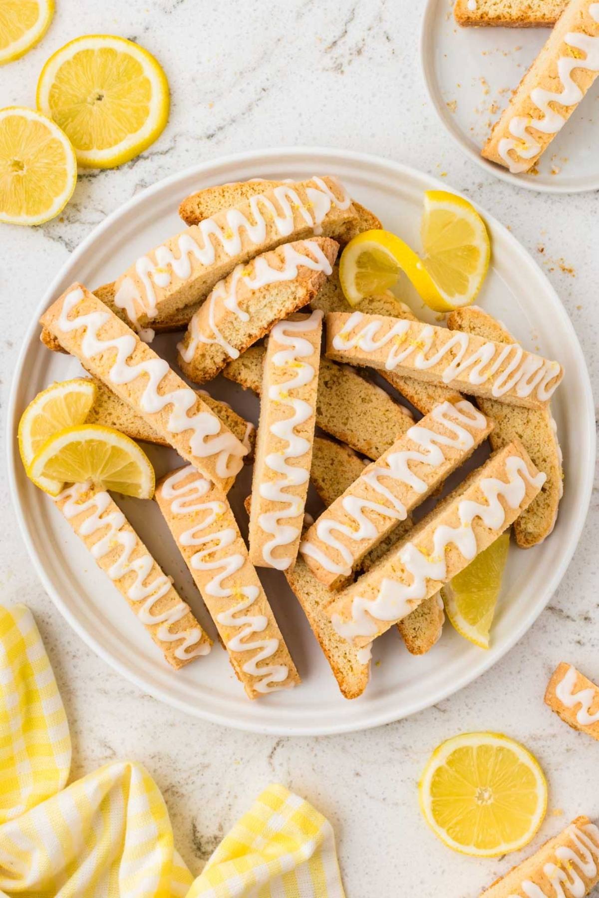 Plate of lemon biscotti with icing drizzle, garnished with lemon slices on a white surface.
