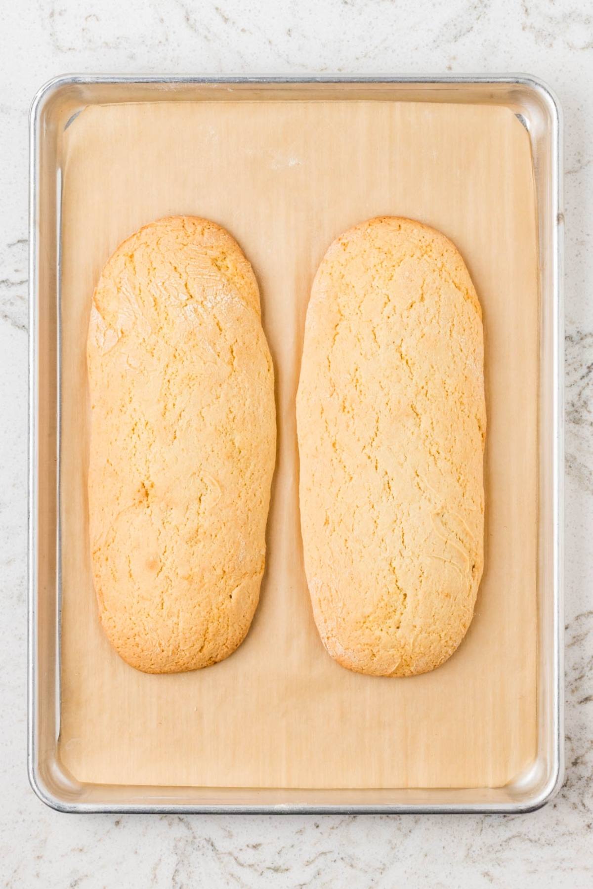 Two oval-shaped loaves of baked bread on a parchment-lined baking sheet.