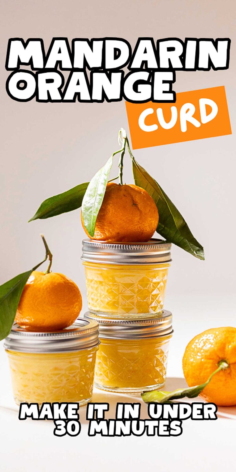 Three jars of mandarin orange curd are stacked, topped and surrounded by fresh mandarins and vibrant green leaves.