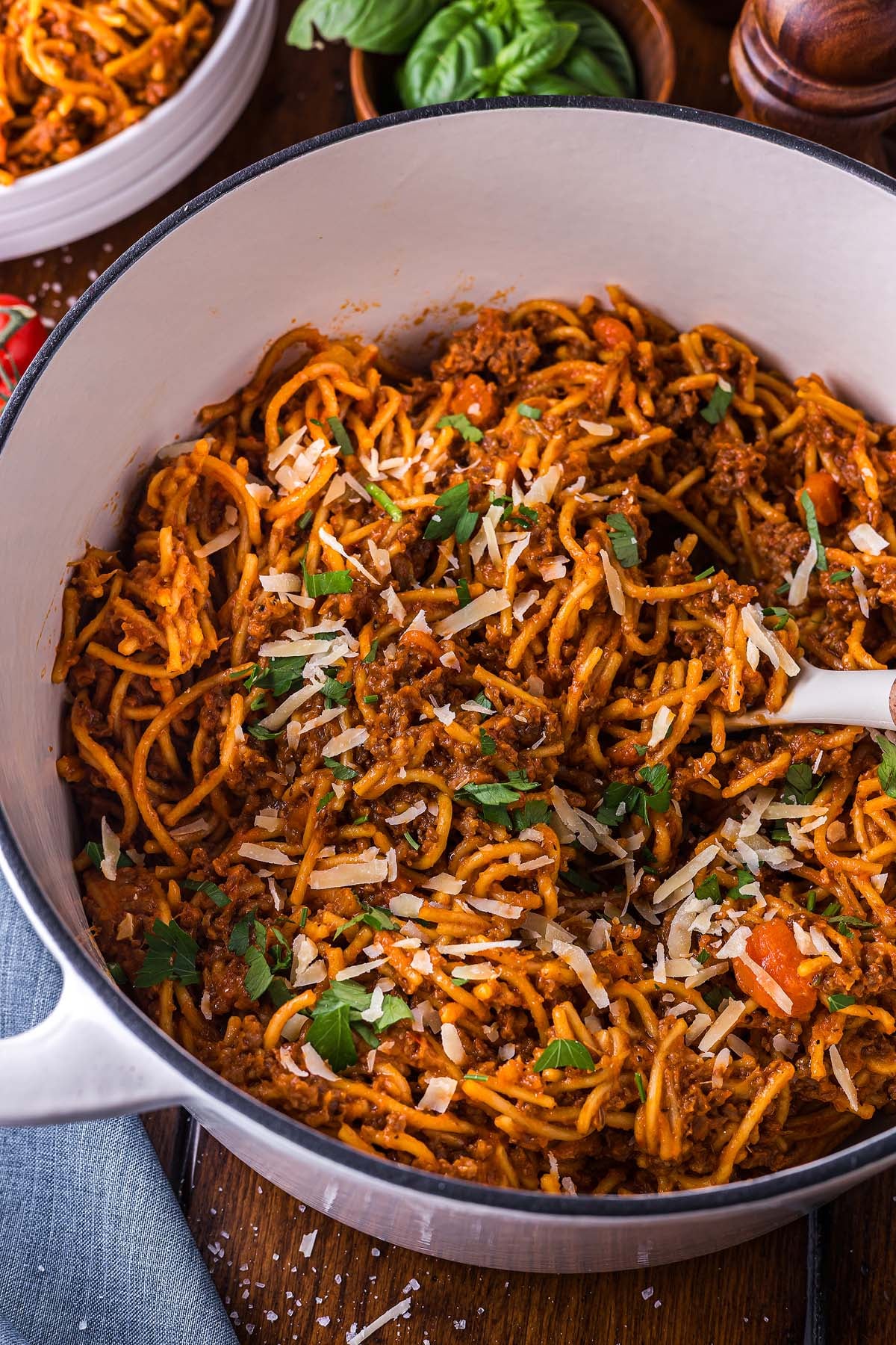 Cooked one pot pasta with meat sauce, topped with grated cheese and parsley, served in a white pot with a serving spoon.