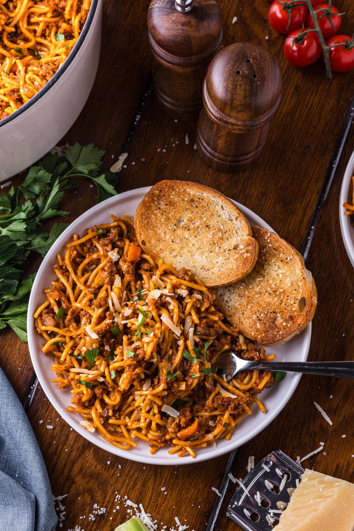 A plate of One pot pasta spaghetti with meat sauce, topped with herbs, served with two slices of toasted bread.