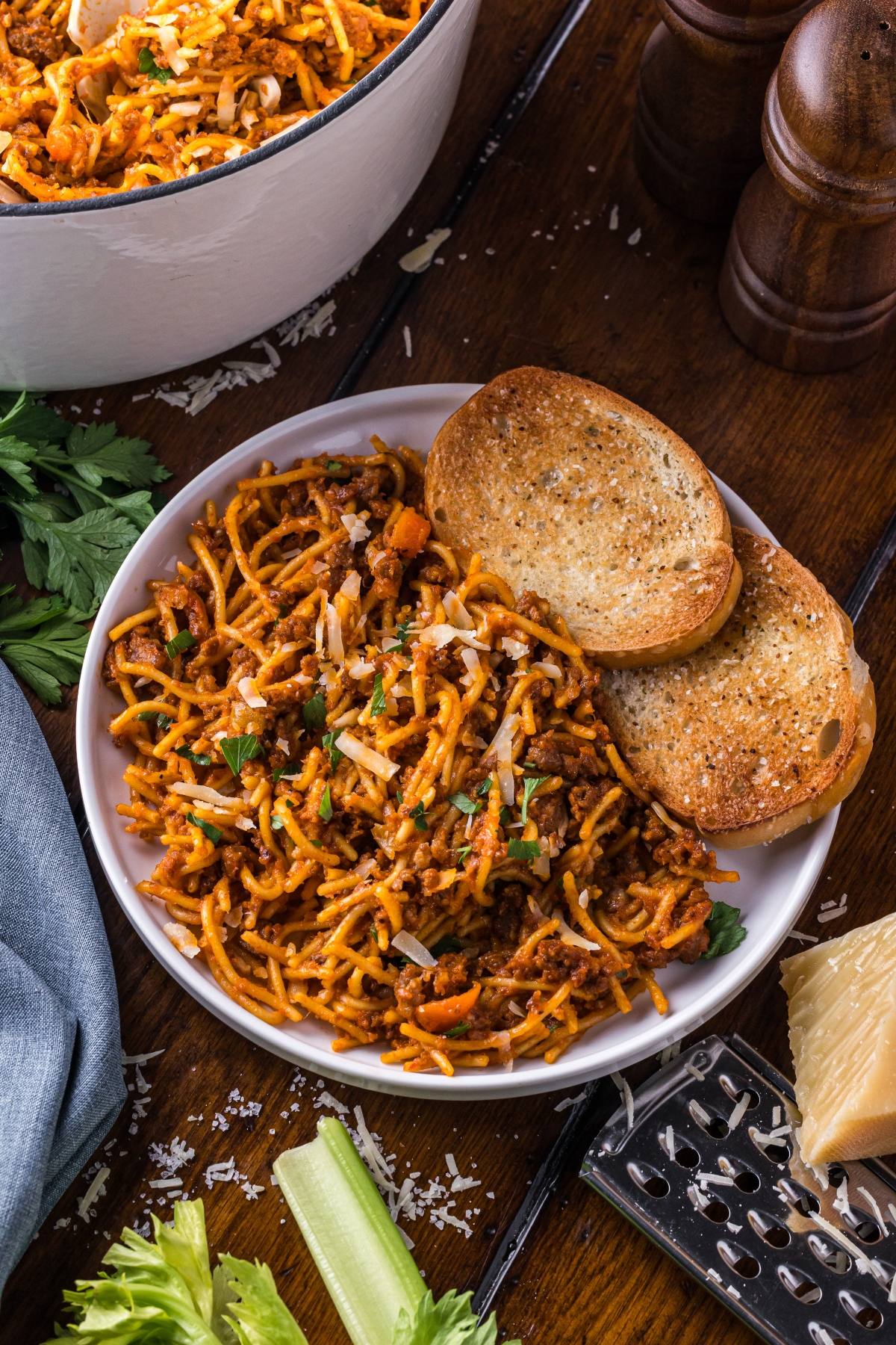 A plate of One pot pasta  spaghetti with meat sauce and two slices of toasted bread on a wooden table.