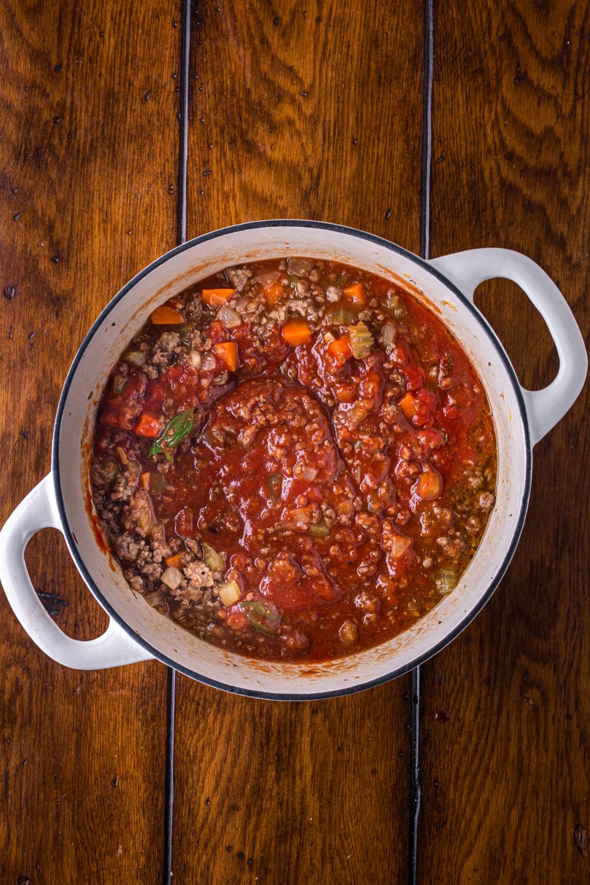 A pot of hearty meat and vegetable tomato stew sits on a wooden table.