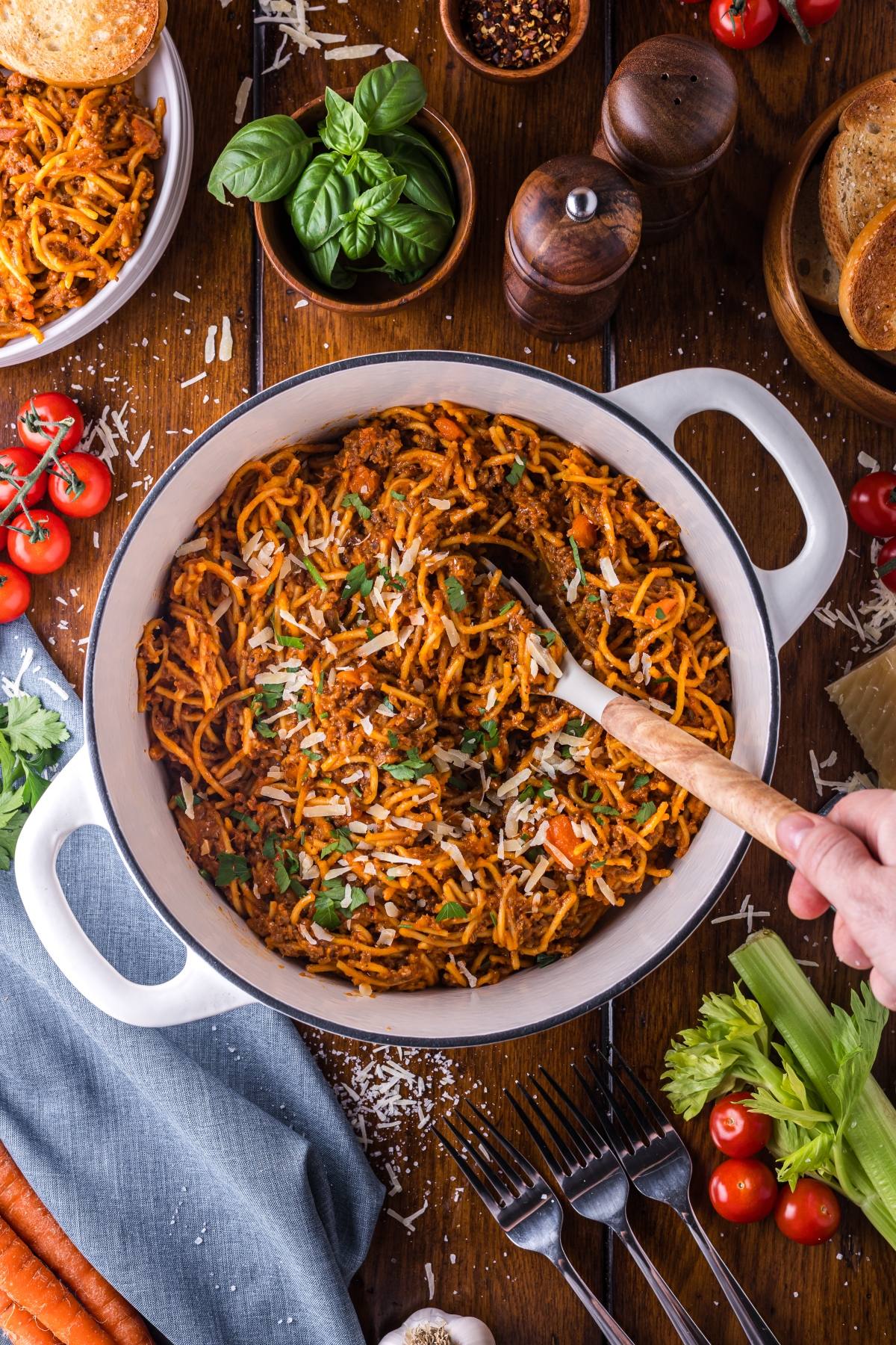 A One pot pasta of spaghetti with meat sauce topped with cheese and herbs, surrounded by fresh vegetables and bread.
