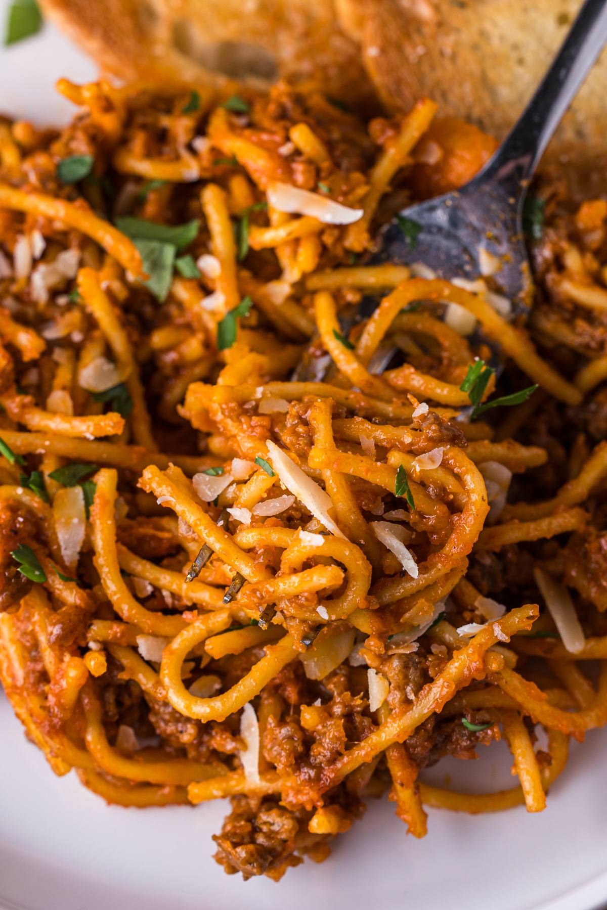 Close-up of One pot pasta  spaghetti with meat sauce, garnished with parsley and grated cheese, with a fork and bread.