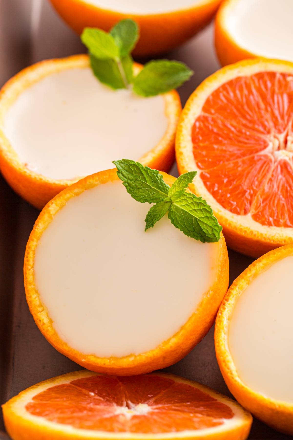 Halved oranges filled with creamy dessert, garnished with mint leaves, with orange slices nearby.