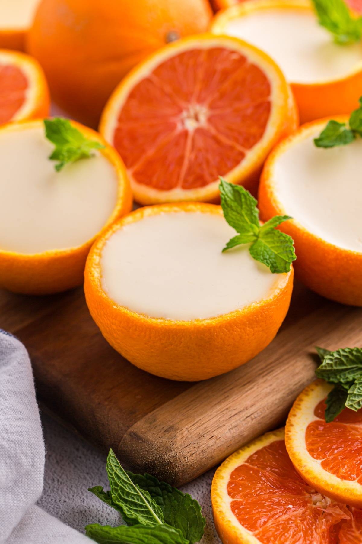 Halved oranges filled with creamy dessert, garnished with mint leaves, on a wooden board with orange slices.