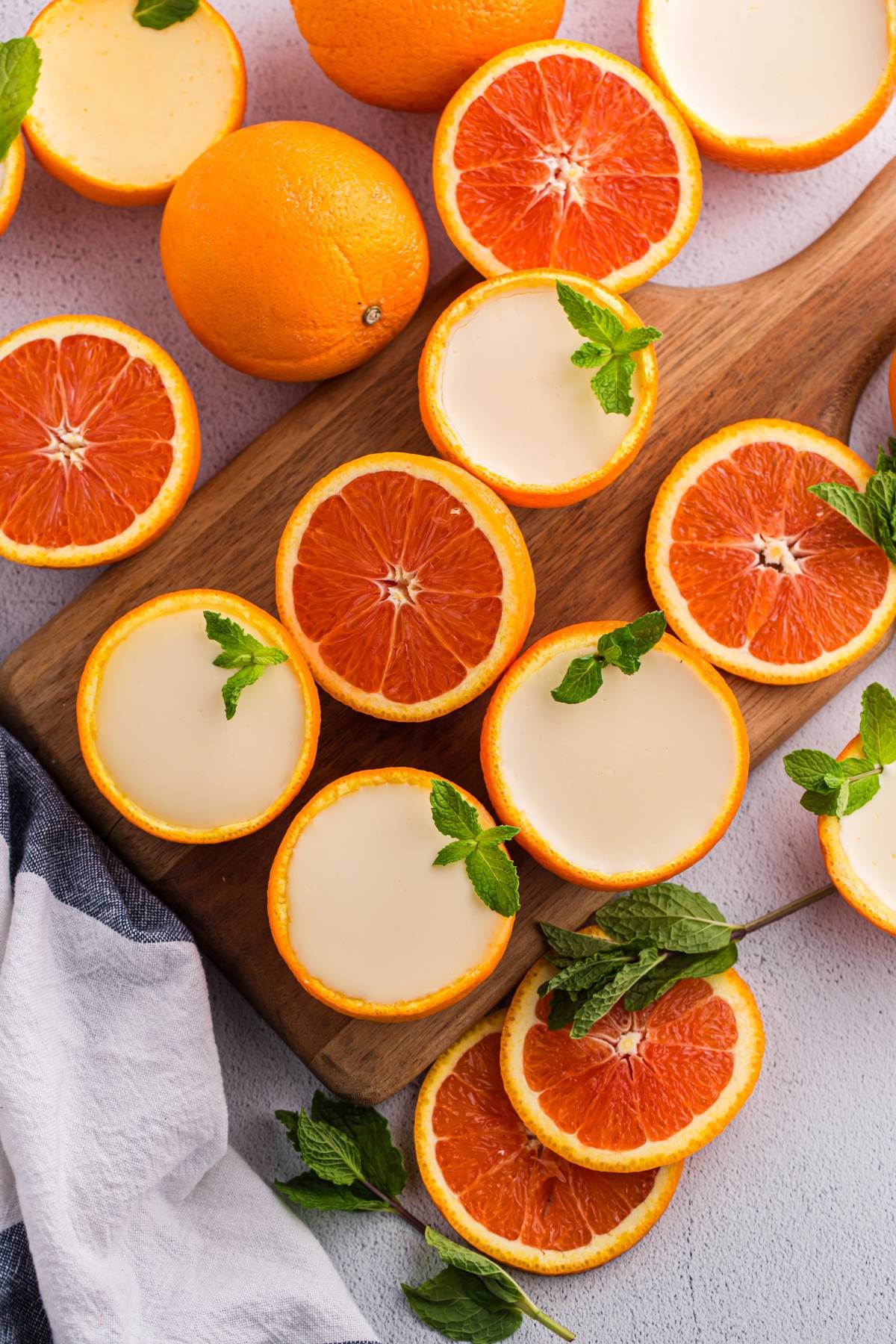 Halved oranges and orange mousse in orange peels, garnished with mint, on a wooden board.