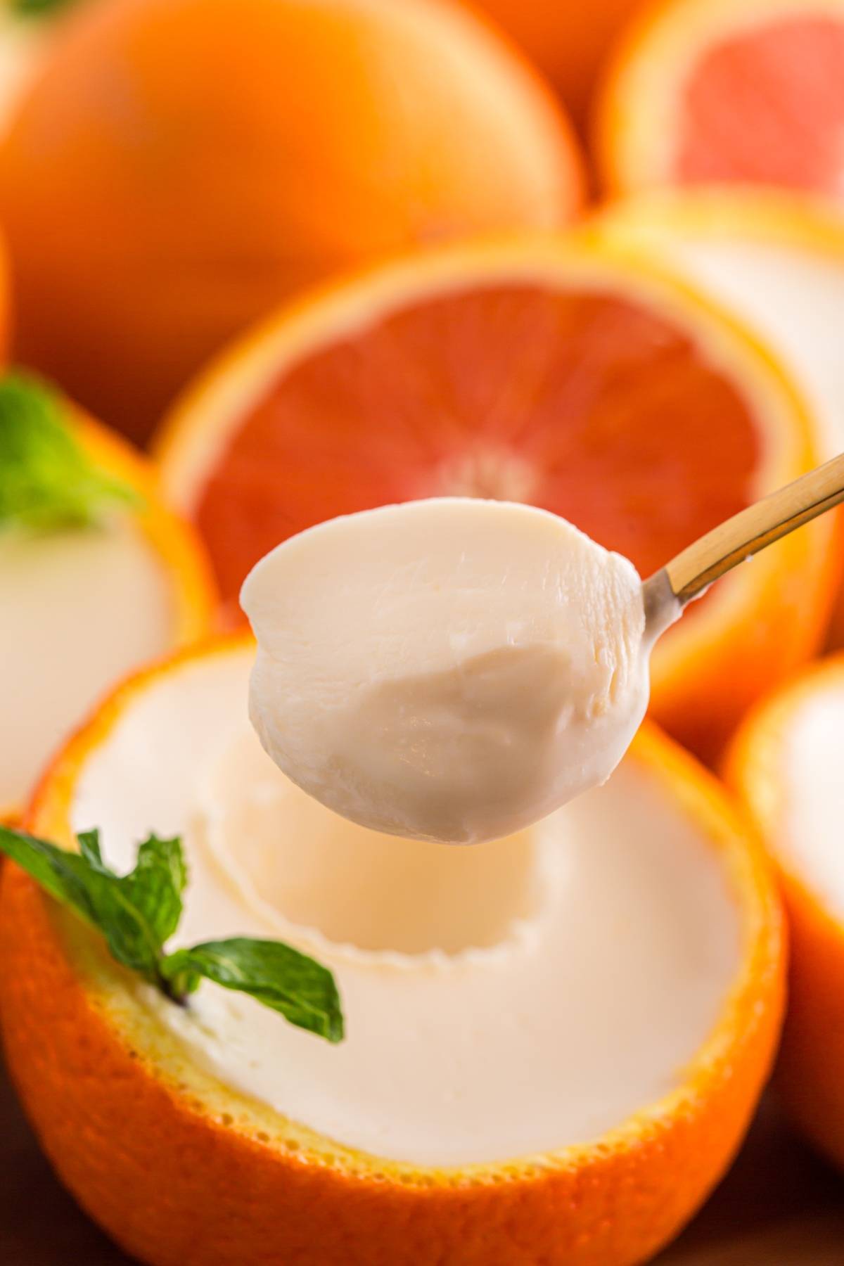 A spoonful of creamy dessert above an orange posset half filled with the same dessert, garnished with mint.