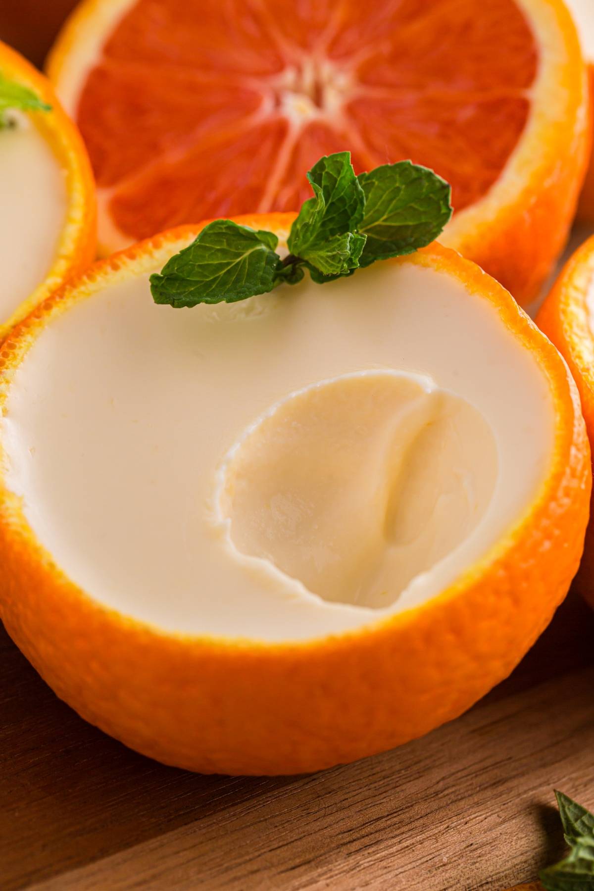 Orange posset halves filled with creamy dessert, garnished with mint leaves, on a wooden surface.
