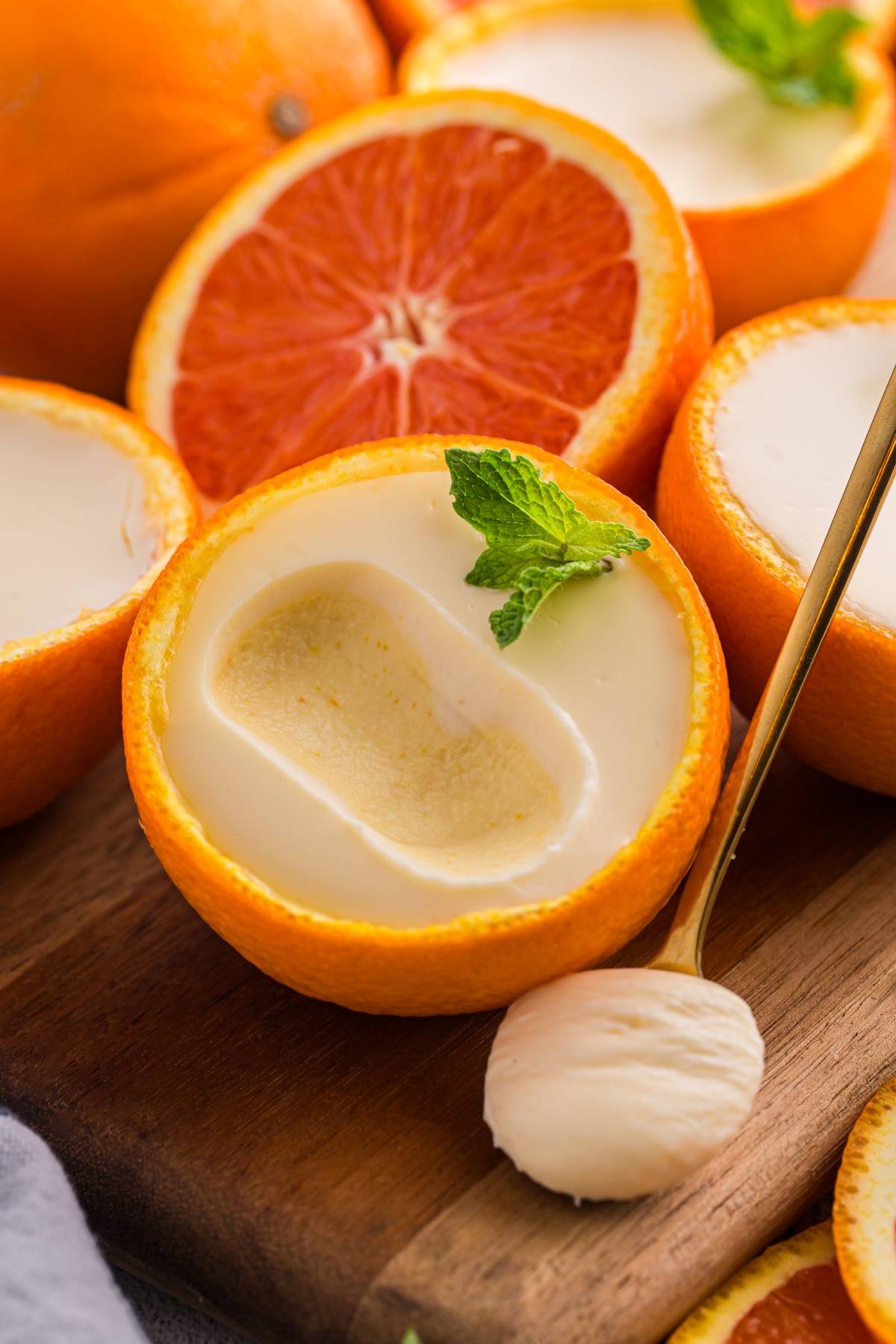 Creamy dessert served in an orange posset peel bowl, garnished with mint, with a spoonful beside it.