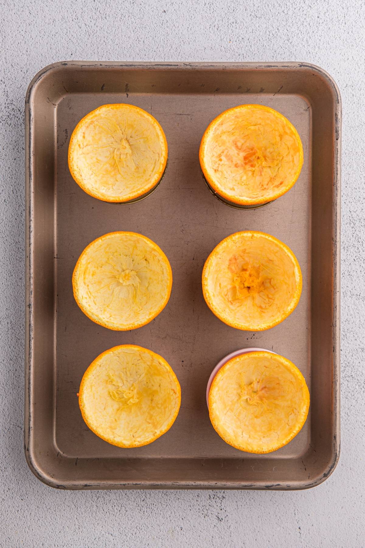 Six hollowed-out squash halves arranged on a metal baking sheet on a light countertop.