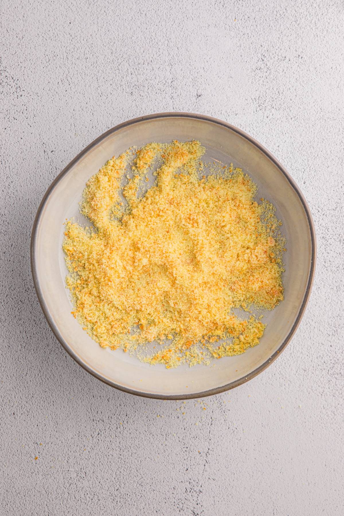 A grey bowl filled with yellow cornmeal on a light textured surface.